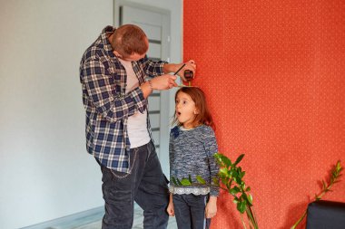 Baba, kızın boyunu evdeki duvarla karşılaştırıyor, aile hayatı gibi. Boşluğu kopyala.