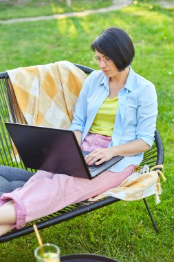 Bilgisayarda uzaktan çalışan bir kadın, dizüstü bilgisayarla çalışan serbest çalışan bir kadın, sosyal medyayı kontrol eden, internetten alışveriş yapan, bahçenin arka bahçesindeki eve sipariş veren bir kadın.