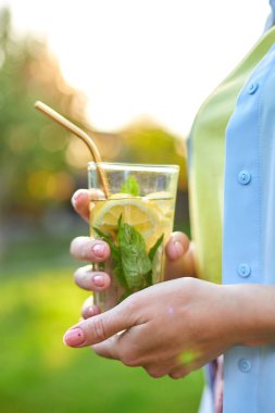 Yaz narencili limonata içen bir kadın soğuk içecek, yaz mevsimi, çevre dostu içecek pipetli, sağlıklı yaşam tarzı, vejetaryen yemeği, detoks suyu olan bir arka bahçe evinde yeniden kullanılabilir metal pipetlerle parti veriyor.