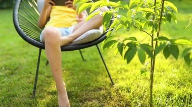 Parkta cep telefonuyla oyun oynayan mutlu bir kız çocuğu ev bahçesinde, arka bahçede akıllı telefon kullanan bir çocuk, güneş ışığı, akıllı telefon bağımlılığı.