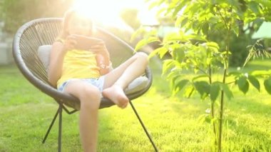 Parkta cep telefonuyla oyun oynayan mutlu bir kız çocuğu ev bahçesinde, arka bahçede akıllı telefon kullanan bir çocuk, güneş ışığı, akıllı telefon bağımlılığı.