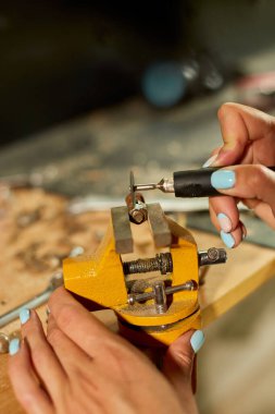 Çalışan bir kadın öğütücü kullanıyor, kadın eli metal bir fındık öğütüyor, atölyede cıvatalar, metal işçiliğinde kıvılcımlar...