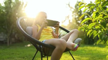 Parkta cep telefonuyla oyun oynayan mutlu bir kız çocuğu ev bahçesinde, arka bahçede akıllı telefon kullanan bir çocuk, güneş ışığı, akıllı telefon bağımlılığı.