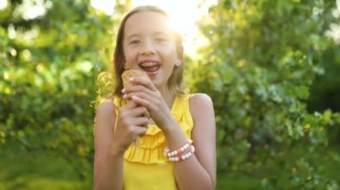 Cute girl with braces eating italian ice cream cone smiling while resting in park on summer day, child enjoying ice cream outdoor, happy holidays, summertime