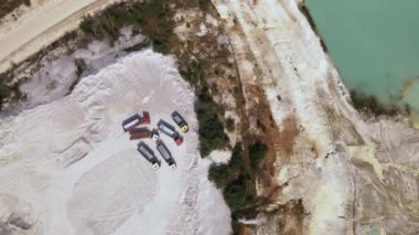 Aerial view trucks near quarry extraction porcelain clay, kaolin, with turquoise water and white shore, drone view open pit mine kaolin flooded with water, Ukraine