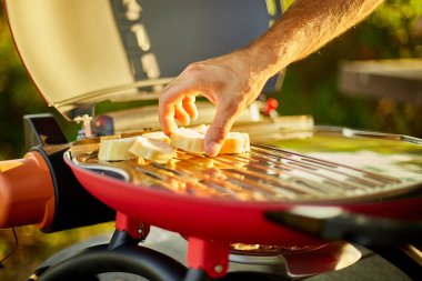 Close up on man's hand put bread, roasting bruschetta on the barbecue gas grill outdoor in the backyard, Breakfast On Grill, summer family picnic, food on the nature.