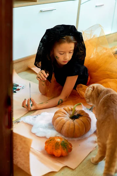 快乐的小女孩在家里用猫装饰南瓜 小女孩在橙色万圣节前夕用南瓜画着脸 假日装饰概念 — 图库照片