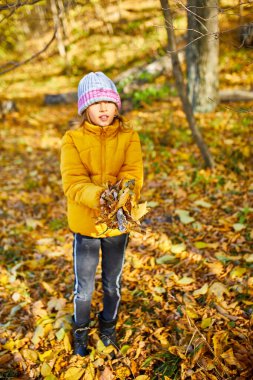 Happy adorable child girl laughing and playing yellow fallen leaves in autumn outdoors, Happy moment