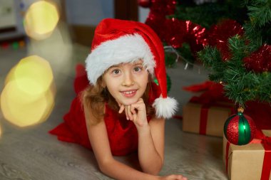 Noel Baba şapkalı mutlu kız evde Noel ağacının yanında yatıyor. Mutlu Noeller ve mutlu tatiller.