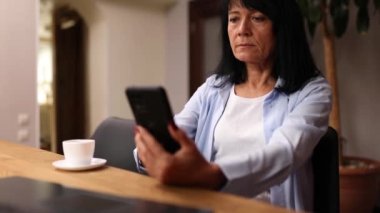 Yaşlı bayan iş kadını işyerinde dinleniyor, cep telefonu kullanıyor ve mesai saatlerinde kahve içiyor. Kadın işte dinleniyor.