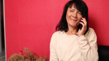 Orta yaşlı, beyaz bir kadın, arkadaşlarıyla, torunlarıyla, iş arkadaşlarıyla telefonda konuşuyor, cep telefonuyla evde akıllı telefonlar, koltukta oturan şık, yaşlı bir kadın.,