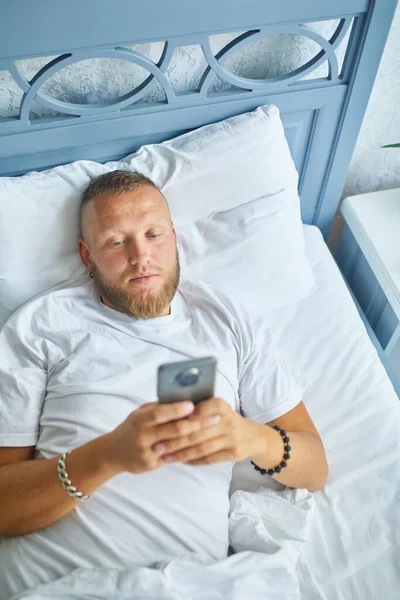 Skäggig Man Med Hjälp Smartphone Morgonen Mysiga Medan Liggande Sängen — Stockfoto