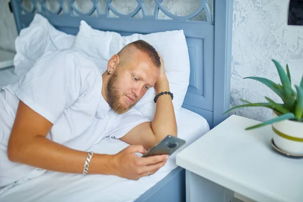 Skäggig Man Med Hjälp Smartphone Morgonen Mysiga Medan Liggande Sängen — Stockfoto