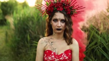Uzun kırmızı elbiseli güzel cadı çiçek çemberi, açık havada kırmızı duman, Santa Muerte karnavalı Cadılar Bayramı, Azizler Günü, Cadılar Bayramı korkunç konsept,