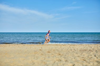 Noel Baba şapkalı mutlu anne ve kız kumsalda koşup eğleniyorlar. Yeni yıl tatilinde aile turistiyim..
