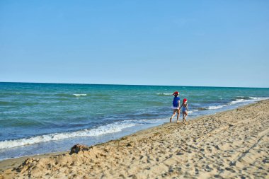 Noel Baba şapkalı mutlu anne ve kız kumsalda koşup eğleniyorlar. Yeni yıl tatilinde aile turistiyim..