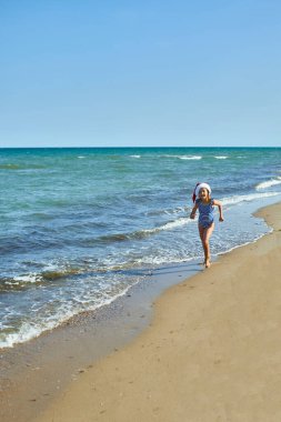 Noel Baba şapkalı mutlu küçük gorl sahilde duruyor. Yeni Yıl Tatili Turisti Denizde.