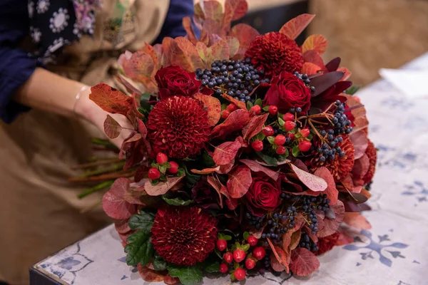 Podzimní koncept kytice červených chryzantémů, červených růží, červených hypericových bobulí, fialových bobulovin a jasných barevných listů v řeckém květinářství v listopadu. — Stock fotografie