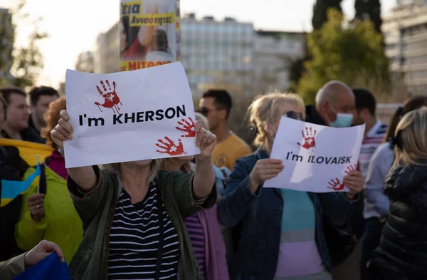 SYNTAGMA SQUARE, ATHEN, GRIECHENLAND - 3. April 2022: Antikriegsprotest zur Unterstützung der Ukraine, Demonstranten halten Plakate im KHERSON und im ILOVAISK Text auf weiß mit roten Handabdrücken hoch. — Stockfoto