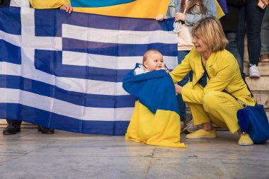 SYNTAGMA KUZAY, ATHENS, GREECE - 3 Nisan 2022: UKRAINE 'daki SAVAŞ' a karşı barışçıl bir protesto için arka planda Ukrayna bayrağına sarılı küçük bir vatansever.
