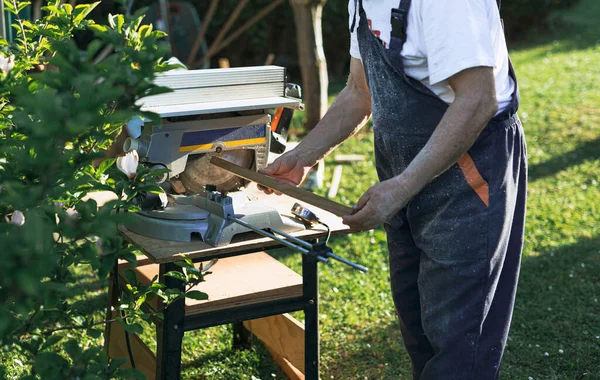 Üst düzey bir adamın elleri, öğleden sonra bahçede kesilecek dairesel bir testere için hazırlanmış ahşap bir yelek taşıyor.