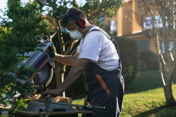 Gri saçlı adam bahçede çalışıyor. Öğleden sonra testere ile.
