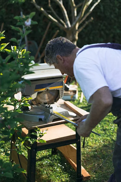 Yetişkin tamirci, bahçeyi kesen dairesel testere için kereste ölçüyor. dikey fotoğraf.