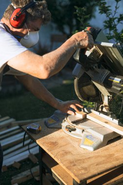 Kıdemli marangozun dairesel bir testereyle odun keserken çekilen dikey detaylı fotoğrafı.