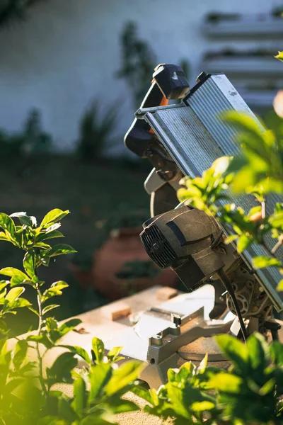 Bahçedeki tezgah üzerinde seçici bir odak ile dairesel testere, saksılar ve beyaz arka plan duvarı arasında odaklanmış