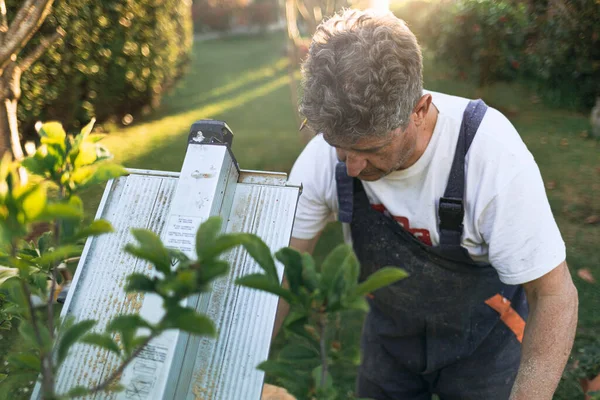 Kulağında kalem olan bir adam bahçedeki testere üzerinde ahşap kesiyor..