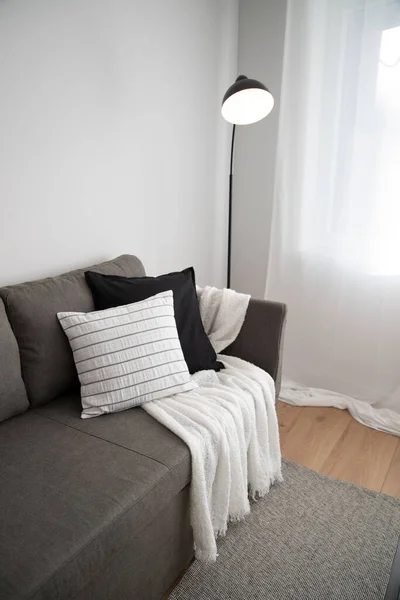 Pencerenin yanında yastıkları olan gri bir kanepenin yanında siyah lamba. dikey.
