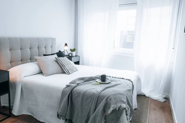 上にコップがあるベッドの横の窓から白い光が差し込むアパートの寝室 不動産シーン — ストック写真