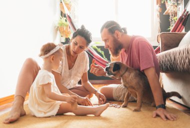 Rus baba ve Venezuelalı anne kızlarıyla oturma odasında oynuyorlar ve yanlarında köpekleri var.