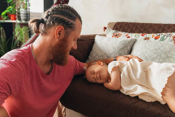 Babası kızıl sakallı, bebeğine bakıyor. Kanepede gülümsüyor ve onu uyutuyor.