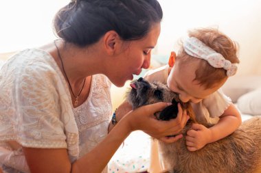 latina mother and daughter hugging and kissing their small breed dog