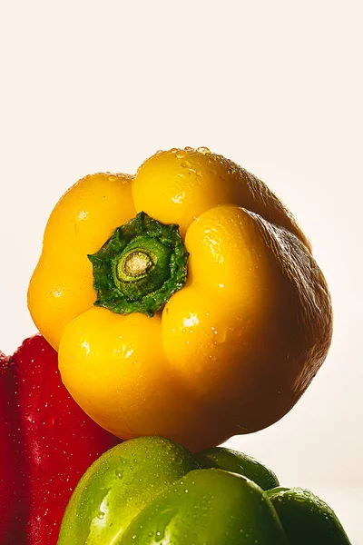 photograph of green, red and yellow peppers wet and stacked on a white background