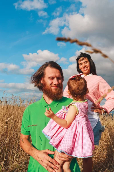 Mutlu, genç bir aile eğleniyor ve gülümsüyor. Birbirlerine doğal bir manzarada bakıyorlar.