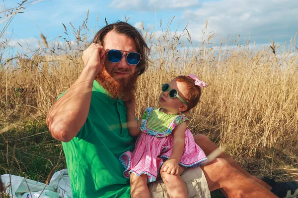 Uzun saçlı babası ve kızıl saçlı küçük beyaz kızı güneşli bir günde eğleniyor ve şık ve serin güneş gözlüğü takıyor.