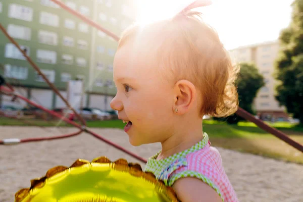 Güler yüzlü kızıl saçlı kız güneşli bir günde parkta altın bir balonla oynuyor.