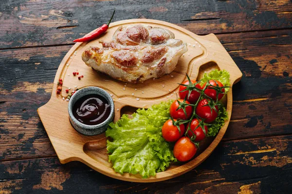 Χοιρινή μπριζόλα σε ξύλινη σανίδα με ντοματίνια και σαλάτα. Ρουστίκ τρόφιμα — Φωτογραφία Αρχείου