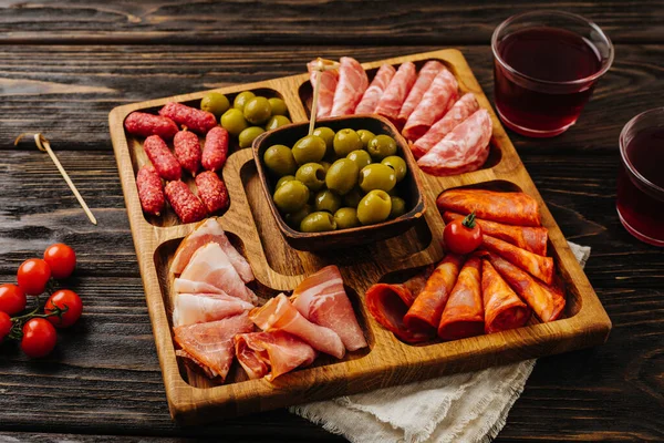 Makanan ringan untuk anggur di papan kayu. Menazhnitsa dengan sosis, zaitun dan tomat ceri. Stok Gambar