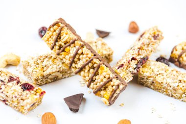 Beyaz arka plan üzerinde fındık, tohum, siyah çikolata, bal ve böğürtlen içeren çeşitli ev yapımı granola barların yakın görüntüsü.