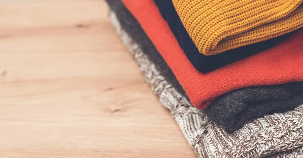 Temiz yün giysiler üst tarafta. Ahşap arka planda örülmüş kalın giysiler. Renkli kıyafetler, eski tarz. Süveter yığını masanın üstünde. Sonbahar, kış örgü giysileri.