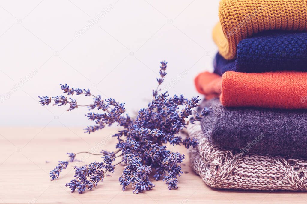 Woolen sweaters and dried lavender for protection from moth. Knitted warm wool clothes. Stack of warm knitted clothes with lavender. Home wardrobe with winter clothes. Autumn, winter season knitwear.