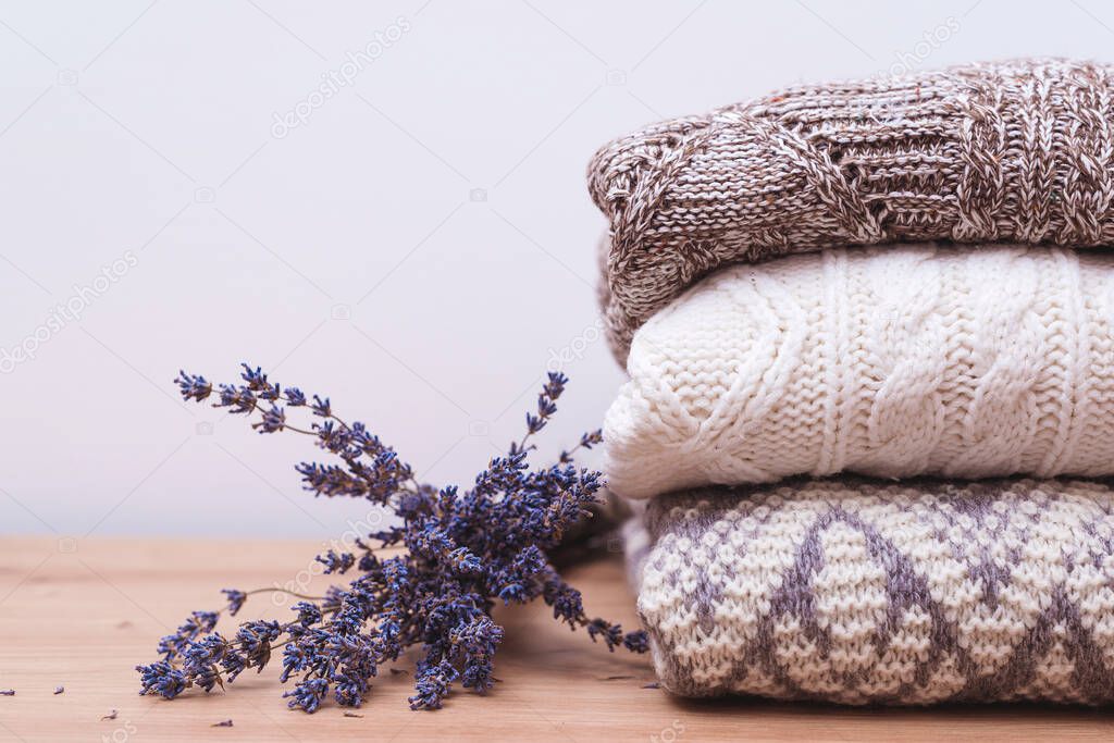 Home wardrobe with winter clothes. Woolen sweaters and dried lavender for protection from moth. Knitted warm wool clothes. Stack of warm knitted clothes with lavender. Autumn, winter season knitwear.