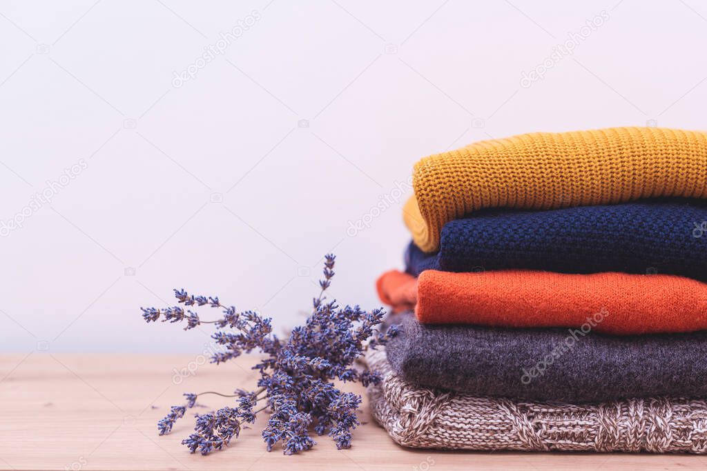 Autumn, winter season knitwear. Woolen sweaters and dried lavender for protection from moth. Knitted warm wool clothes. Stack of warm knitted clothes with lavender. Home wardrobe with winter clothes.