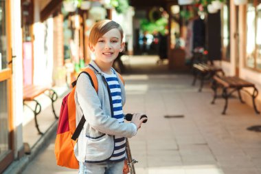 Okul konseptine geri dönelim. Şık ceket giyen mutlu okul çocuğu. Sırt çantalı çocuk okula gidiyor. Sokakta gezen mobileti olan şık bir çocuk..