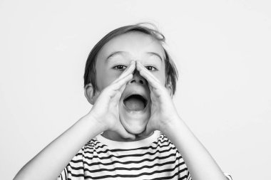 Çocuk ağzını iyice açıyor ve ellerini yanaklarından tutuyor. Çocuk bağırıyor. Duygularınla ve ifadenle yüzleş. Beyaz arka planda bağıran sevimli bir çocuk..