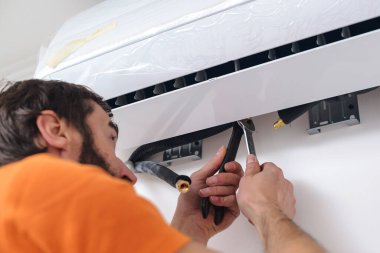 İşçi daireye yeni bir klima takıyor. İnşaat, bakım ve onarım konsepti. Modern klimayı kapalı alanda çalıştıran profesyonel bir teknisyen..