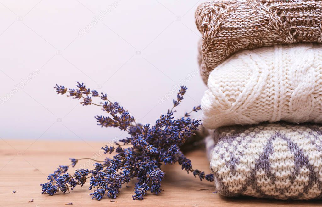 Stack of warm knitted clothes with lavender. Woolen sweaters and dried lavender for protection from moth. Home wardrobe with winter clothes. Autumn, winter season knitwear. Knitted warm wool clothes.